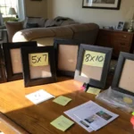 Overhead view of a messy table with frames, rulers, and photos being sorted by hand — frame size guide